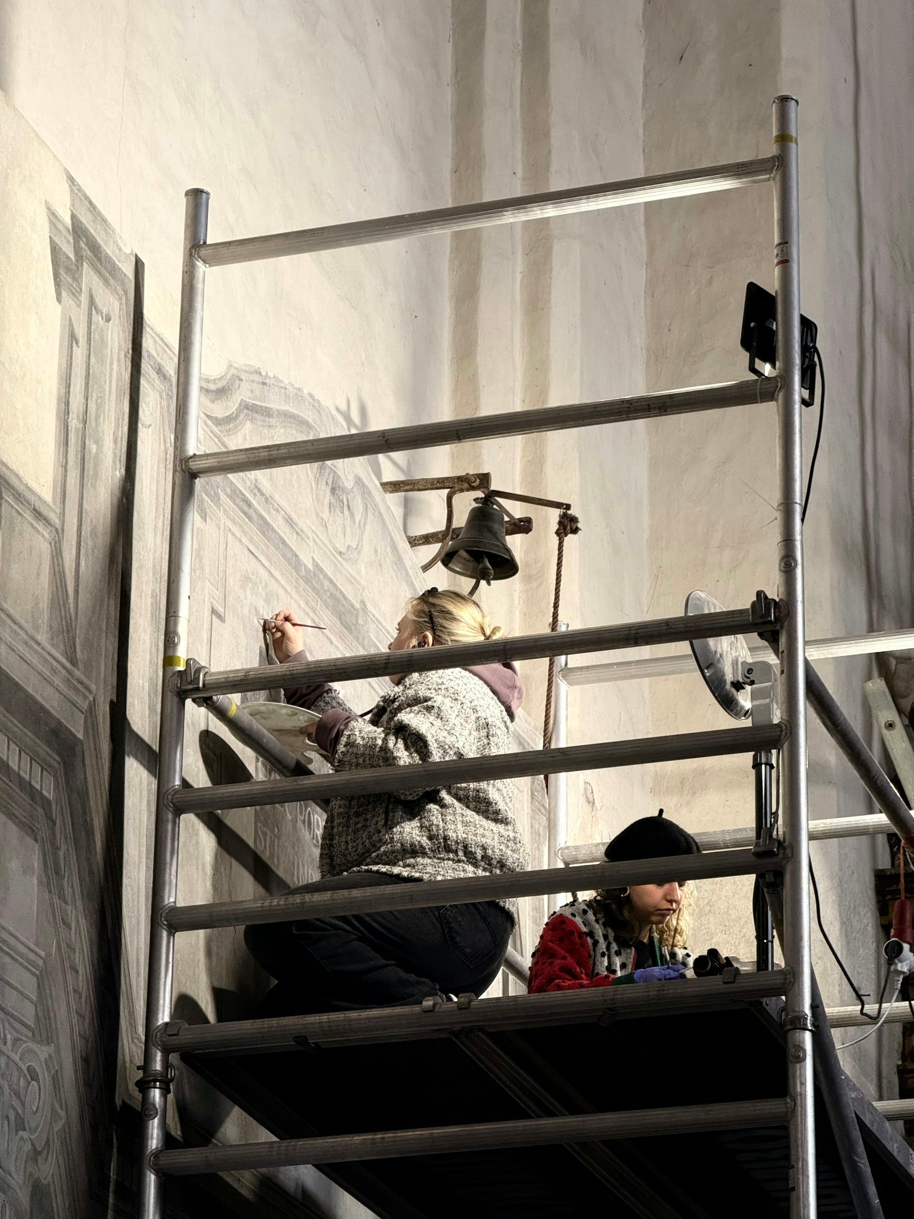 Conservators restoring a large historic mural from scaffolding